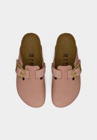 Ζευγάρι ροζ παπούτσια τύπου clog με χρυσά αγκράφες και καφέ επενδεδυμένες σόλες, σε μέγεθος 38, τοποθετημένα σε λευκό φόντο.