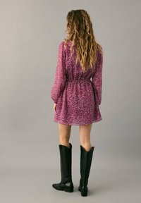 Robe à motifs paisley violets avec manches longues et taille élastique, associée à des bottes noires montantes. Tissu doux et coupe fluide.