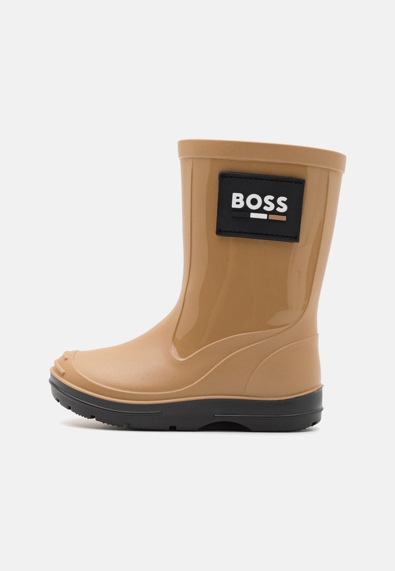 Botte en caoutchouc imperméable de couleur beige avec un patch logo noir portant l'inscription "BOSS". Présente un bout rond, une semelle texturée et une finition lisse.