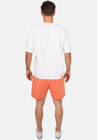 Witte T-shirt met korte mouwen, ontspannen pasvorm, gecombineerd met oranje shorts, van katoen, met een effen ontwerp, en witte sneakers.