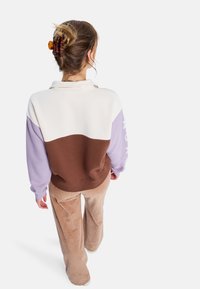 Sweatshirt ve výrazném barevném bloku, skládající se z bílých, levandulových a hnědých odstínů, s límcem a volným střihem. Spárováno s béžovými kordovými kalhotami.