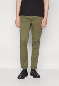 Chinos verde oliva con vestibilità slim, caratterizzati da una texture liscia e design a cinque tasche, abbinati a scarpe nere stringate.
