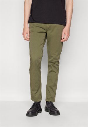 Chinos verde oliva con vestibilità slim, caratterizzati da una texture liscia e design a cinque tasche, abbinati a scarpe nere stringate.