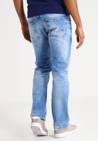 Ljusblå denimjeans med en urtvättad finish, slim fit, femfickorsdesign och subtila sömmar. I kombination med beige sneakers.