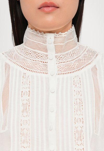 Blusa blanca de cuello alto con detalles de encaje, rayas verticales y cierre de botón en la parte delantera, con un delicado cuello en forma de ondas.