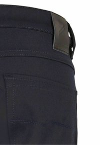 Pantalons bleu foncé au toucher doux, dotés de détails de couture et d'une étiquette en cuir à la taille avec un logo. Le design de la poche arrière est visible.