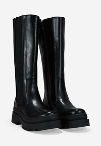 Botas de cuero negras hasta la rodilla con suelas gruesas, cremallera lateral y paneles elásticos, en posición vertical sobre un fondo blanco.