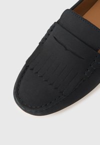 Crni gležnjači od brušene kože s detaljem resica i vidljivim šavovima na bijeloj podlozi, prikazujući gornji prednji dio cipela.