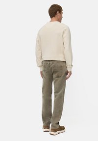 Beige sweatshirt med ribbede manchetter, parret med olivengrønne afslappede jeans med baglommer og subtil falming. Brune sneakers.