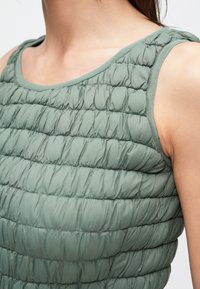 Groene, donzige mouwloze top met een doorgestikte, gewatteerde textuur en smalle, horizontale stiksels. Gladde stof met een ronde halslijn.