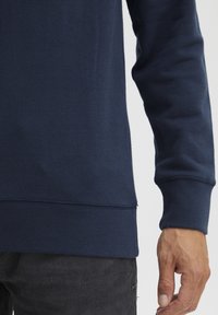 Marineblå hettegenser laget av myk bomull, med ribbestrikket mansjett og kant, har en jevn tekstur og minimale sømdetaljer.