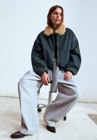 Jeans bomber jakna z umetnim krznom okoli vratu, široke sive trenirke in rjave čevlje z ostrim nosom. Preprost dizajn, sproščen kroj in mehki materiali.