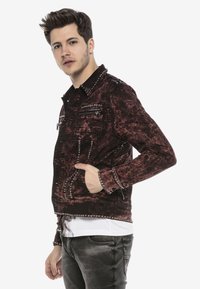 Rote und schwarze, distressed Jeansjacke mit silbernen Nieten, Reißverschlusstaschen und umgeschlagenem Kragen. Slim-Fit-Design mit langen Ärmeln.