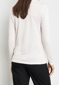 Lätt, krämfärgad långärmad topp med en slät textur och enkel design, kombinerad med svarta byxor.