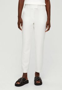 White tapered trousers with a smooth texture, featuring a belt and side pockets, paired with black cross-strap sandals.