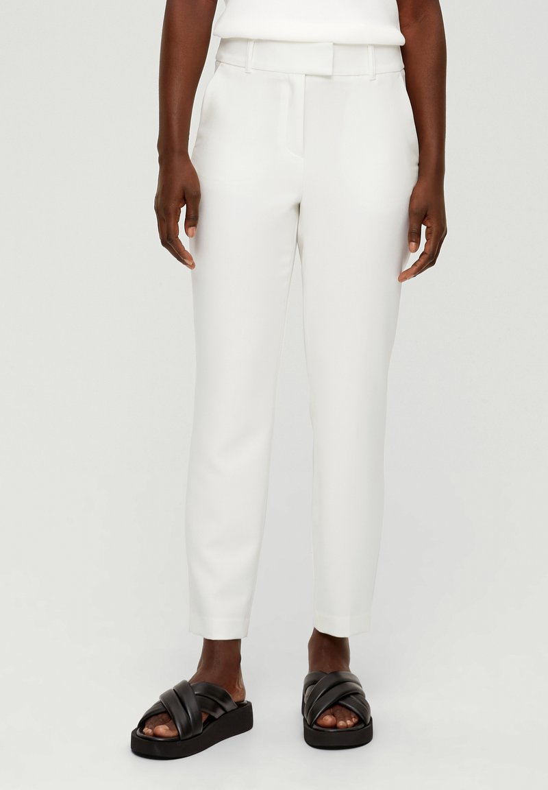 White tapered trousers with a smooth texture, featuring a belt and side pockets, paired with black cross-strap sandals.