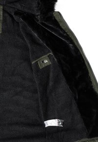 Svart konstpälsfoder inuti en jacka med en olivgrön utsida. Har en liten ficka och en tagg. Mjuk textur, hel dragkedja.