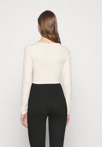 Langärmeliges Oberteil aus offweißem, geripptem Stoff mit tailliertem Schnitt und Rundhalsausschnitt, kombiniert mit hoch taillierten schwarzen Hosen.