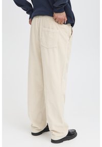 Beige corduroy pants with a relaxed fit, featuring a back pocket, and paired with black shoes. Texture is ribbed and soft.
