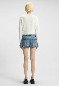 Vit fluffig kortärmad tröja i kombination med en blå denim mini kjol som har en utsvängd nederkant och fem fickor. Svarta platåskor.