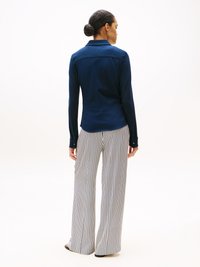 Camisa de manga comprida azul marinho com colarinho, apresentando uma costura traseira limpa e botões. Combinada com calças largas listradas em azul marinho e branco.
