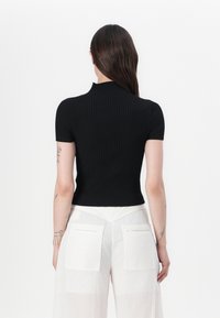Svart stripete kortermet topp med høy hals, figursydd design og teksturert stoff, sammen med lyse vide bukser.