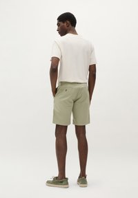 Tricou bej deschis și pantaloni scurți oliv cu buzunare. Pantalonii scurți au o textură netedă și un design curat, fiind asortați cu pantofi slip-on verzi.