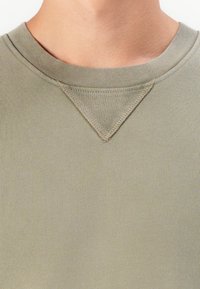Sudadera verde oliva con cuello redondo acanalado y un patrón de acento triangular en el escote. Tejido suave y texturizado con un aspecto ajustado.