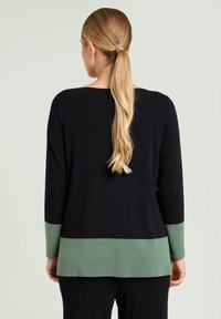 Zwarte trui met lange mouwen, voorzien van een groene ribbelpaneel aan de onderrand. Gladde textuur, iets losvallende pasvorm, recht gesneden ontwerp.