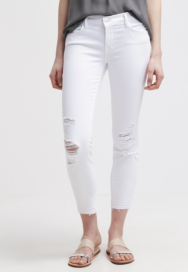 Vaqueros blancos desgastados con roturas en las rodillas, corte slim, cintura media y dobladillo deshilachado. Combinados con sandalias planas en beige y plata.