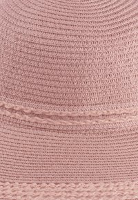 Jasnoróżowy, pleciony kapelusz ze słomy z teksturowanym wykończeniem oraz dekoracyjną, plecioną wstążką wokół korony dla dodatkowego detalu.