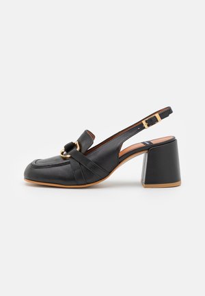 Zapatos de tacón con tiras traseras de cuero negro, punta cuadrada, banda decorativa y adorno de herraje en tono dorado. Presentan un tacón grueso y cuadrado.