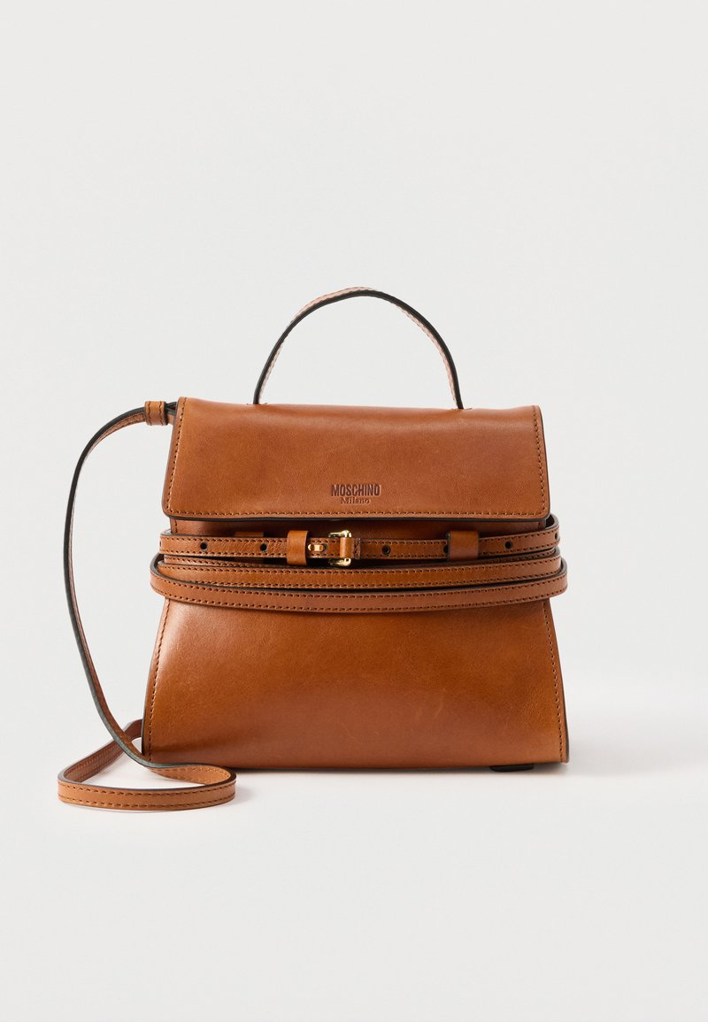 Sac à main en cuir marron avec poignée supérieure et sangle réglable à boucle, logo Moschino Milano sur le rabat avant, posé sur un fond uni.