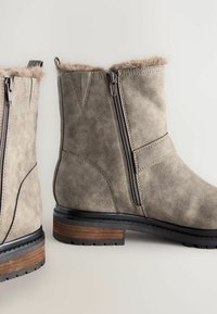 Graue Wildleder-Stiefeletten mit einem Kunstfellkragen, seitlichen Reißverschlüssen und einem gestapelten Holzabsatz. Sie verfügen über gestickte Details und Gummisohlen.