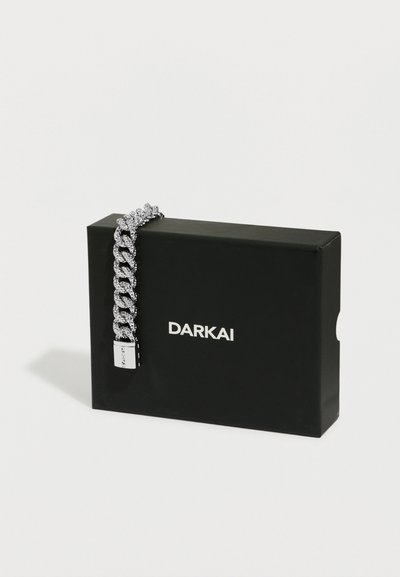 Bracciale a catena spessa d'argento appoggiato su una scatola rettangolare nera con la scritta "DARKAI" stampata in bianco sul davanti.