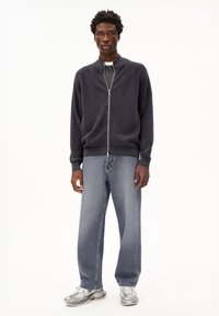 Donkergrijze ritstrui met een gewoven patroon, gecombineerd met lichtblauwe wijde jeans en zilveren sportschoenen.