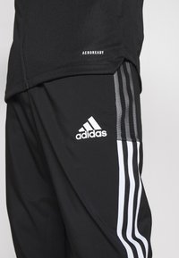 Svarta Adidas träningsbyxor med vit tre-stripes design och logotyp på låret, tillsammans med en svart Aeroready-topp.