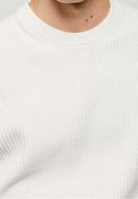 Maglione bianco dalla texture lavorata con un design a costine e collo rotondo. Tessuto liscio con un sottile dettaglio di cucitura.