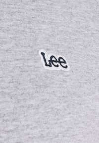 Tessuto grigio del sudore con una texture morbida. Presenta un logo "Lee" ricamato in bianco sul lato sinistro anteriore. Design semplice, senza ulteriori motivi.