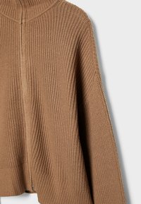 Wafelgebreid, oversized bruin sweater met een hoge kraag, geribbelde textuur en een naaddetail dat langs de achterkant loopt.