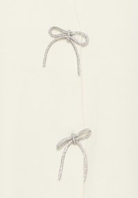 Ivory material z dvema kovinskima srebrnima pentljama na vrhu, ki imata zapletene detajle in gladko teksturo.