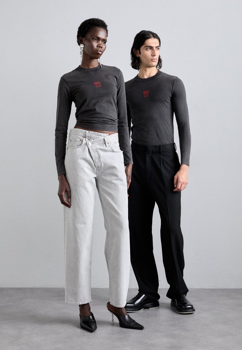 Grau langärmlige T-Shirts mit einem roten Grafikdruck, kombiniert mit hellgrauen weiten Jeans und schwarzen schmal geschnittenen Hosen. Schwarze Absatzmules runden die Looks ab.