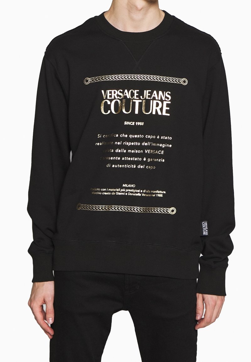Felpa nera in cotone con stampa dorata che presenta "Versace Jeans Couture" e un design decorativo a catena lungo l'orlo e le maniche.
