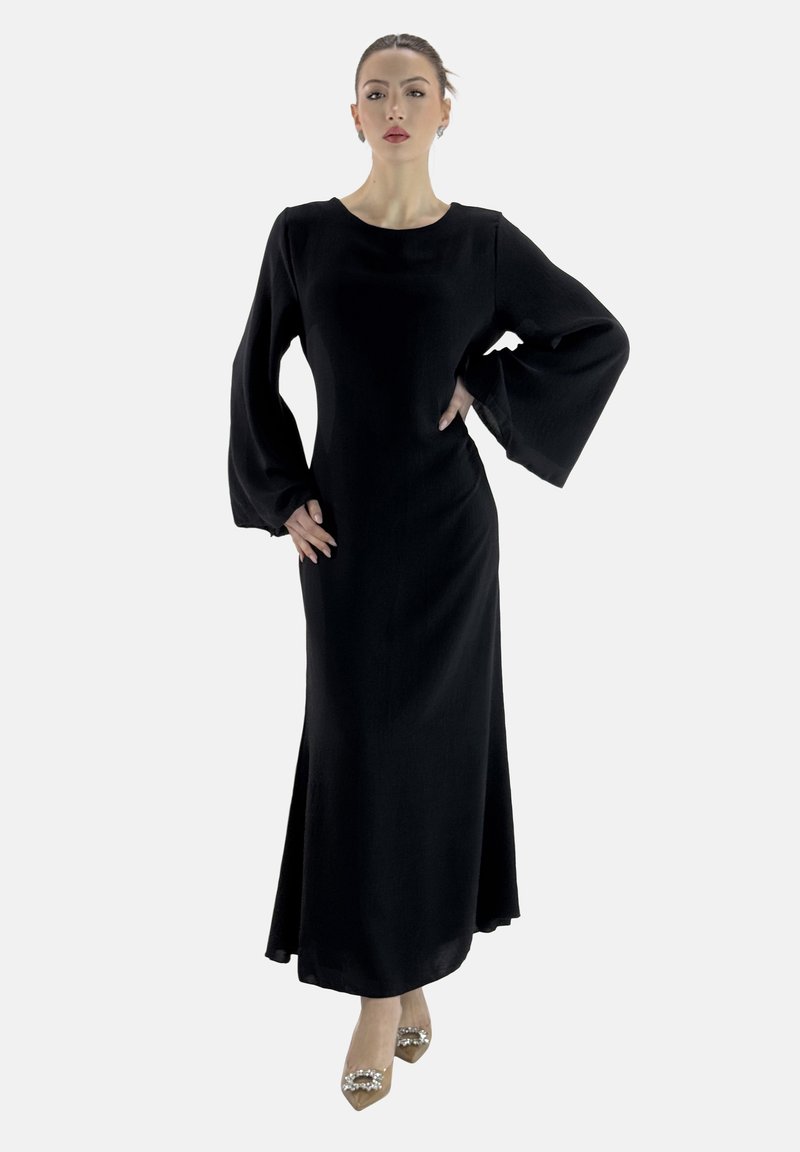 Schwarzes Maxikleid mit langen, Glockenärmeln, aus einem strukturierten Stoff gefertigt. Hat einen runden Halsausschnitt und eine taillierte Silhouette. Trägt verzierten Absatzschuhe.
