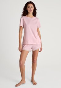 Roze katoenen pyjama-set met een top met korte mouwen en kantdetails, en bijpassende korte broek. Zacht materiaal, comfortabele pasvorm en delicate accenten.