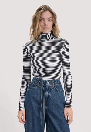 Gestreiftes Rollkragenoberteil in Schwarz und Weiß, taillierte Schnittform mit langen Ärmeln. Getragen mit hoch taillierten blauen Jeans, die einen Bindegürtel besitzen.