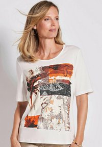 Weißes T-Shirt mit kurzen Ärmeln, das ein buntes Patchwork-Design mit orangefarbenen, braunen und schwarzen Akzenten zeigt, einschließlich Palmen und abstrakten Mustern.