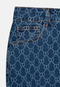 Tissu en denim avec un motif de logo répétitif en bleu clair, featuring coutures orange et un détail de poche arrière au niveau de la taille.