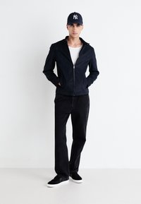 Marineblaue Zip-Up-Jacke mit glatter Textur, schwarze Jeans und schwarze Sneaker mit weißen Sohlen; minimalistisches Design ohne Muster oder Akzente.