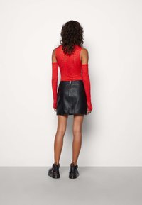 Paita lengan panjang berenda merah dipadukan dengan rok kulit A-line hitam. Penampilan ini memiliki potongan slim fit dan ritsleting di belakang rok.